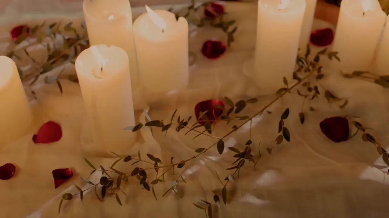 Ljus, rosenblad och gröna kvistar på en vit duk